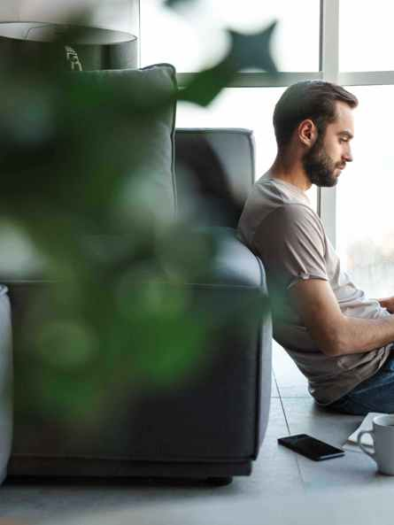 Ihminen istuu lattialla kannettavan tietokoneen ja kahvikupin kanssa